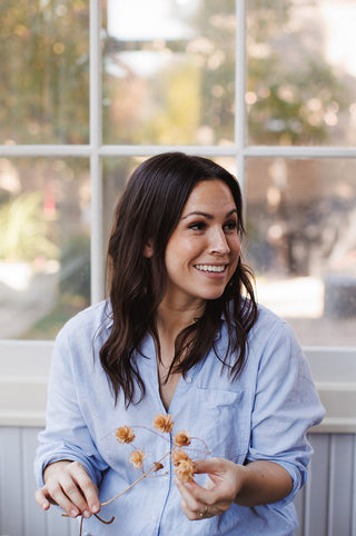 Woman sitting on a chair holding dried flowers in front of a window