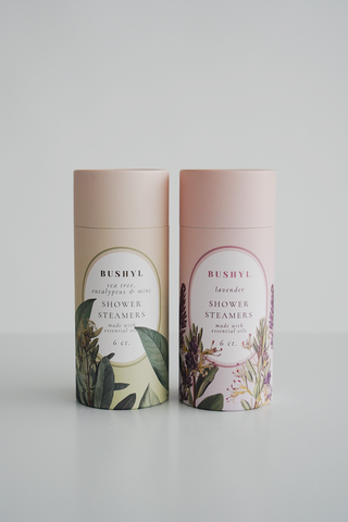 Two cylindrical containers of Bushy Lavender shower steamers on a light gray background